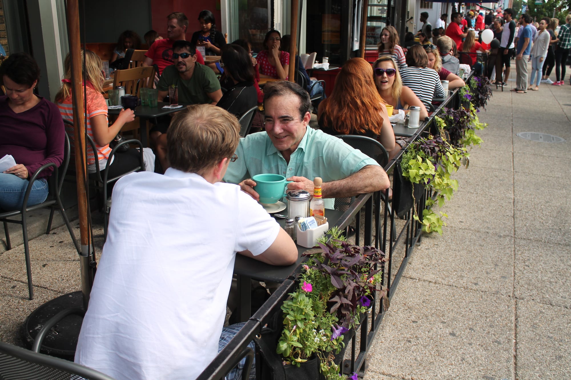 People sitting on a sidewalk cafe in D.C.'s Adams Morgan neighborhood drinking and eating.