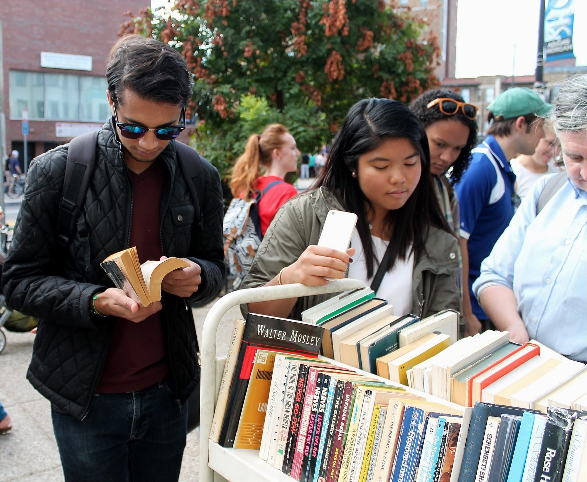 One person is reading a book and another is perusing books on a cart on an outdoor street in D.C.