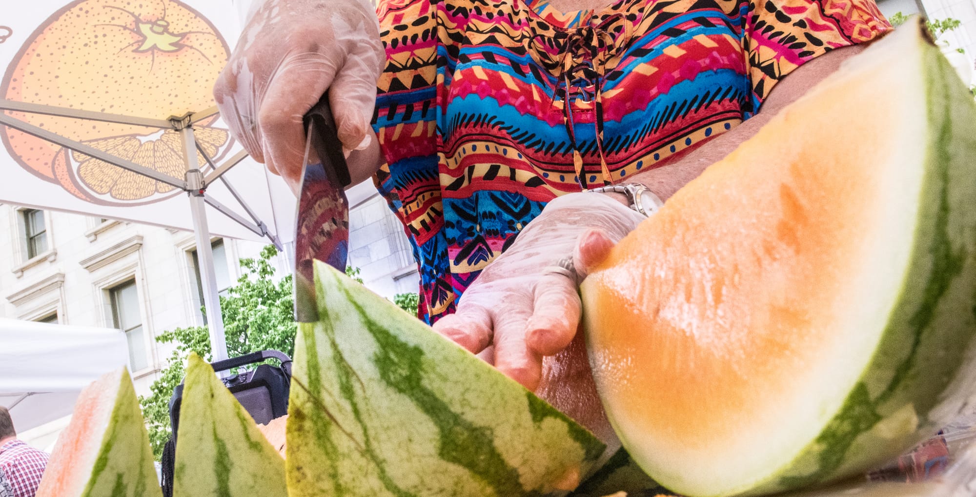 A person in a colorful shirt slices into a yellow watermelon.