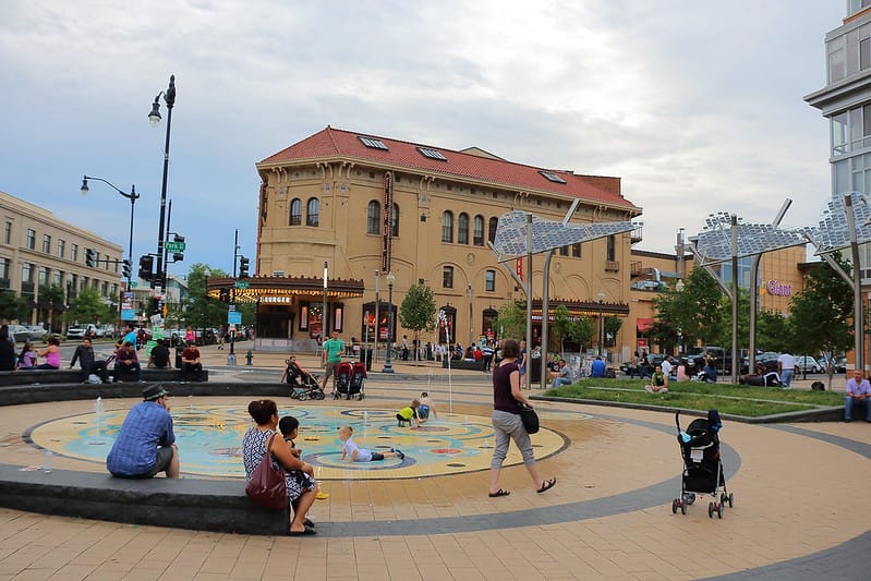 Adults and children scattered at an outdoor plaza surrounded by buildings in Washington D.C.'s Columbia Heights neighborhood.