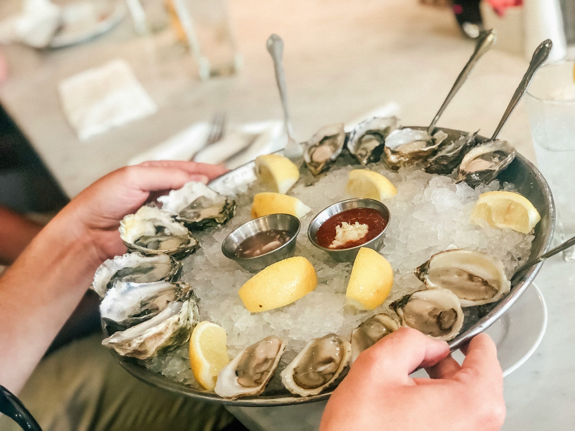 Hands shown holding a plate of oysters over ice. 