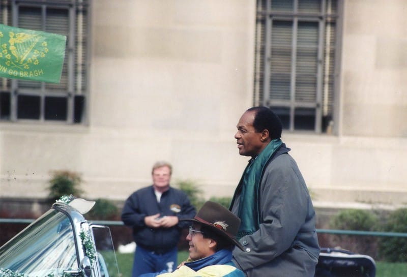 Marion Barry, an African American man, perched on a convertible during a parade.