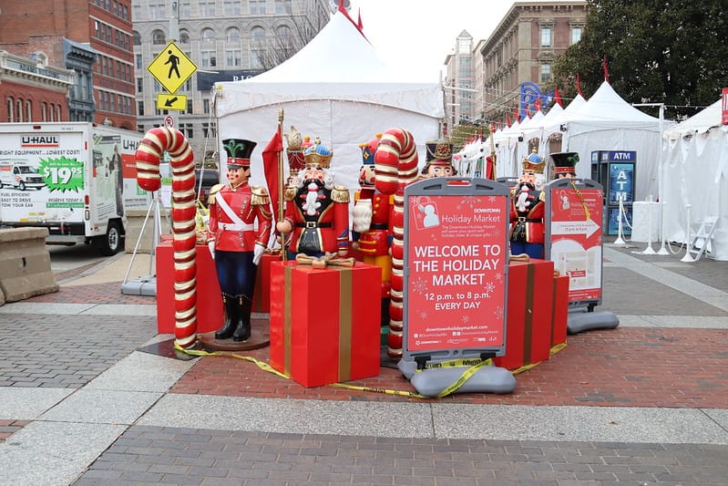 Christmas decor like large candles and gift boxes are gathered outside in front of white tents. 