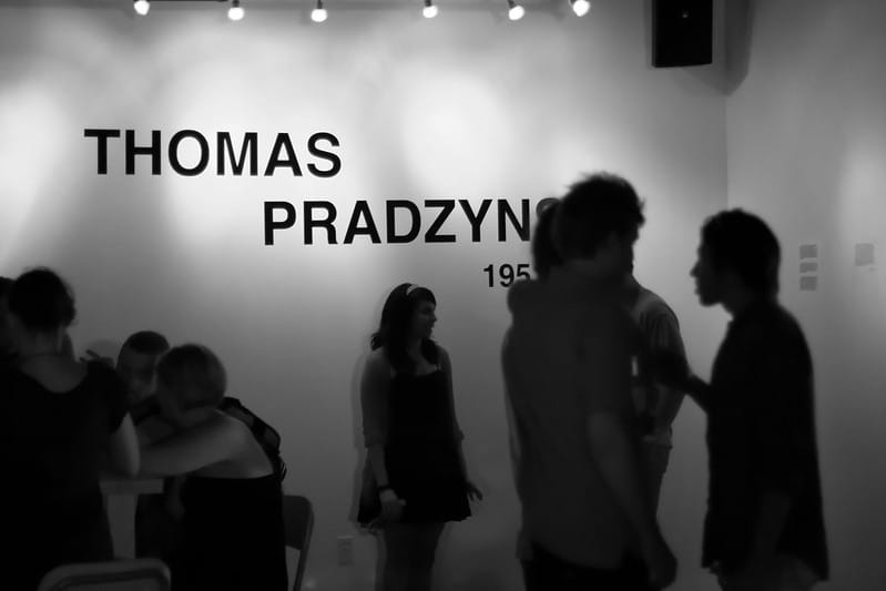 Dark, shadowy figures mingling in a gallery space with the name Thomas written on the wall.