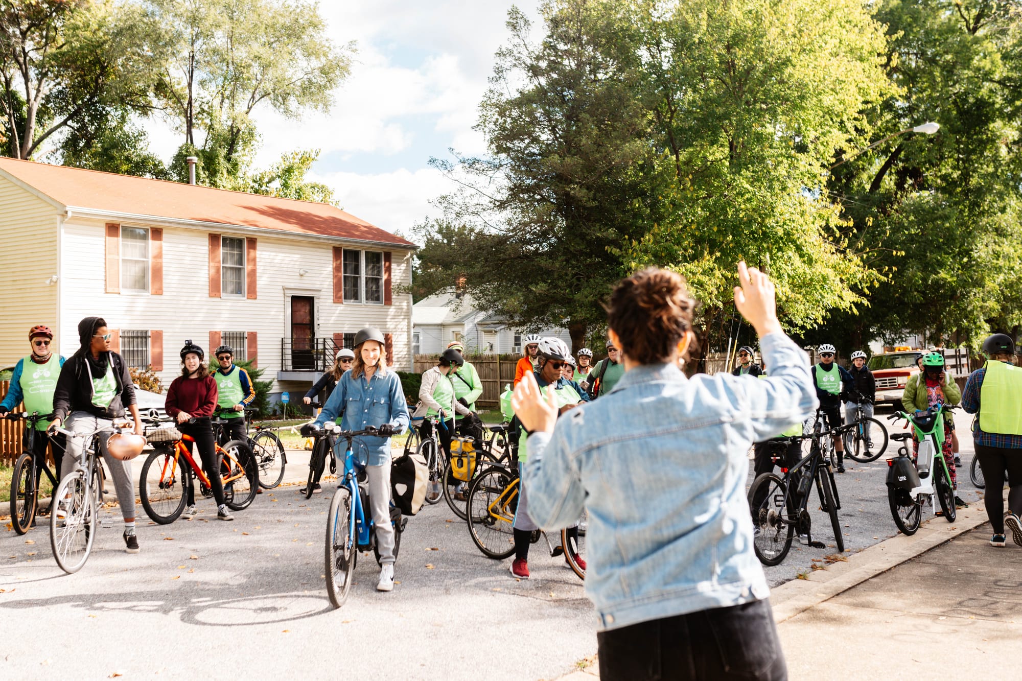 A large group of people on bikes are stopped and waiting for someone in a jean jacket in the foreground to talk.