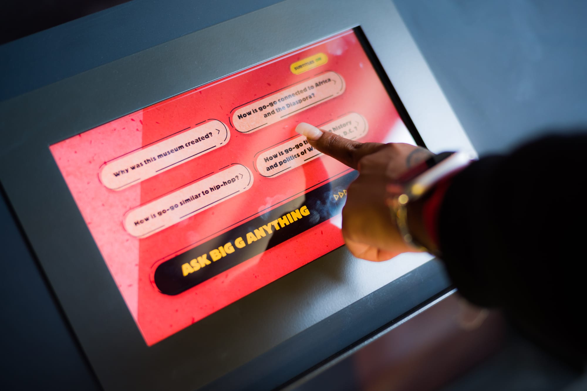 A finger selects an option from a screen at an interactive exhibit. 