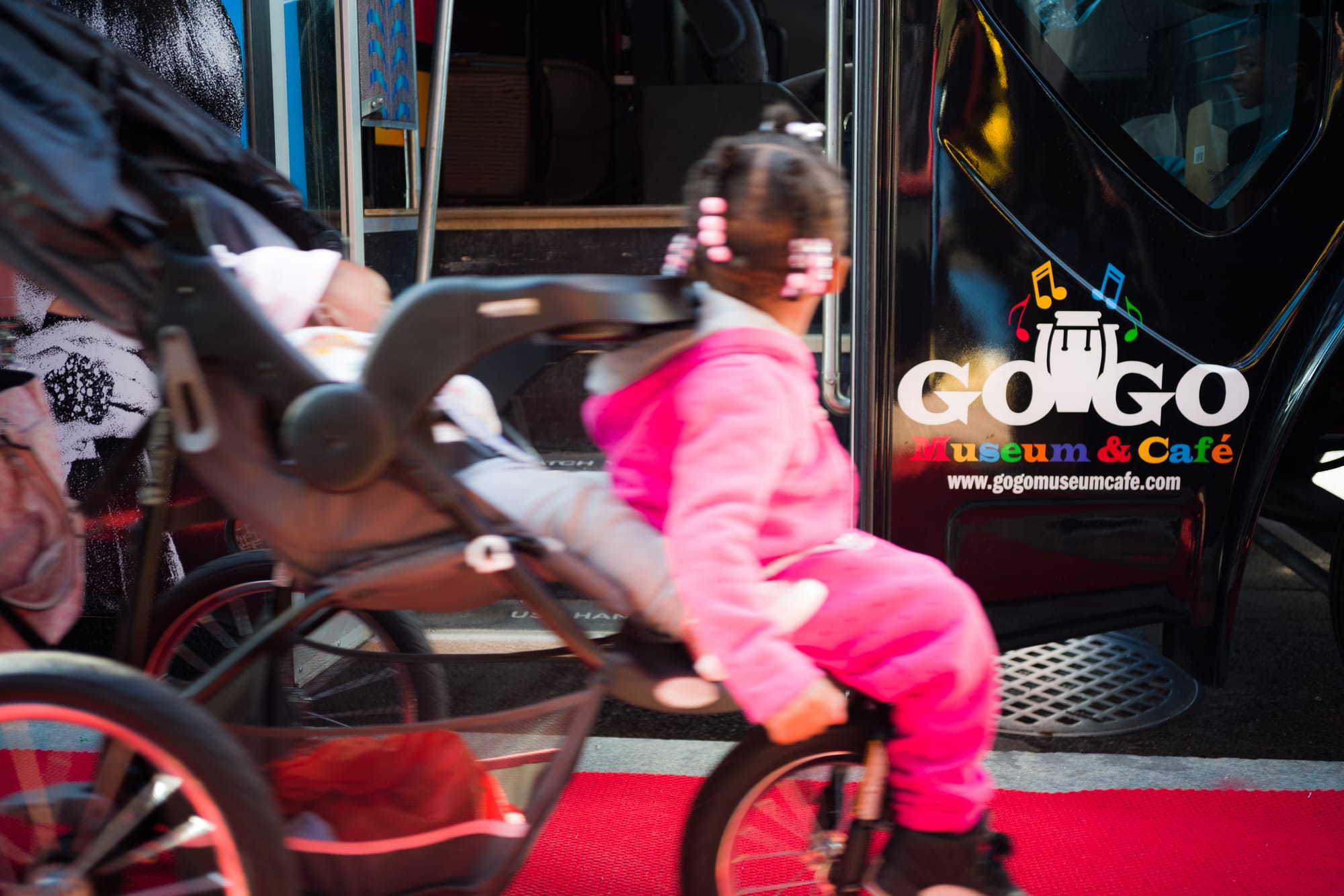 A little girl in a pink jump suit blurs by the a van. 