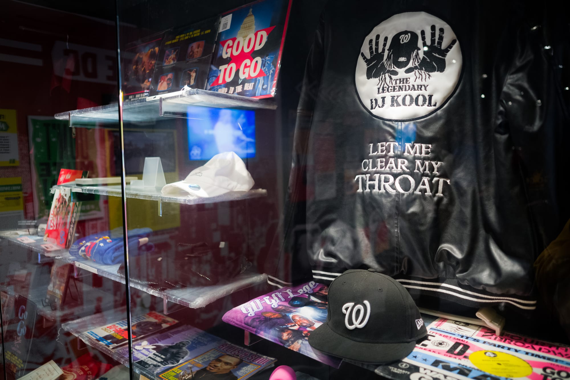 A black Washington National hat sits on a shelf, with a black jacket that reads "The LEGENDARY DJ KOOL." 