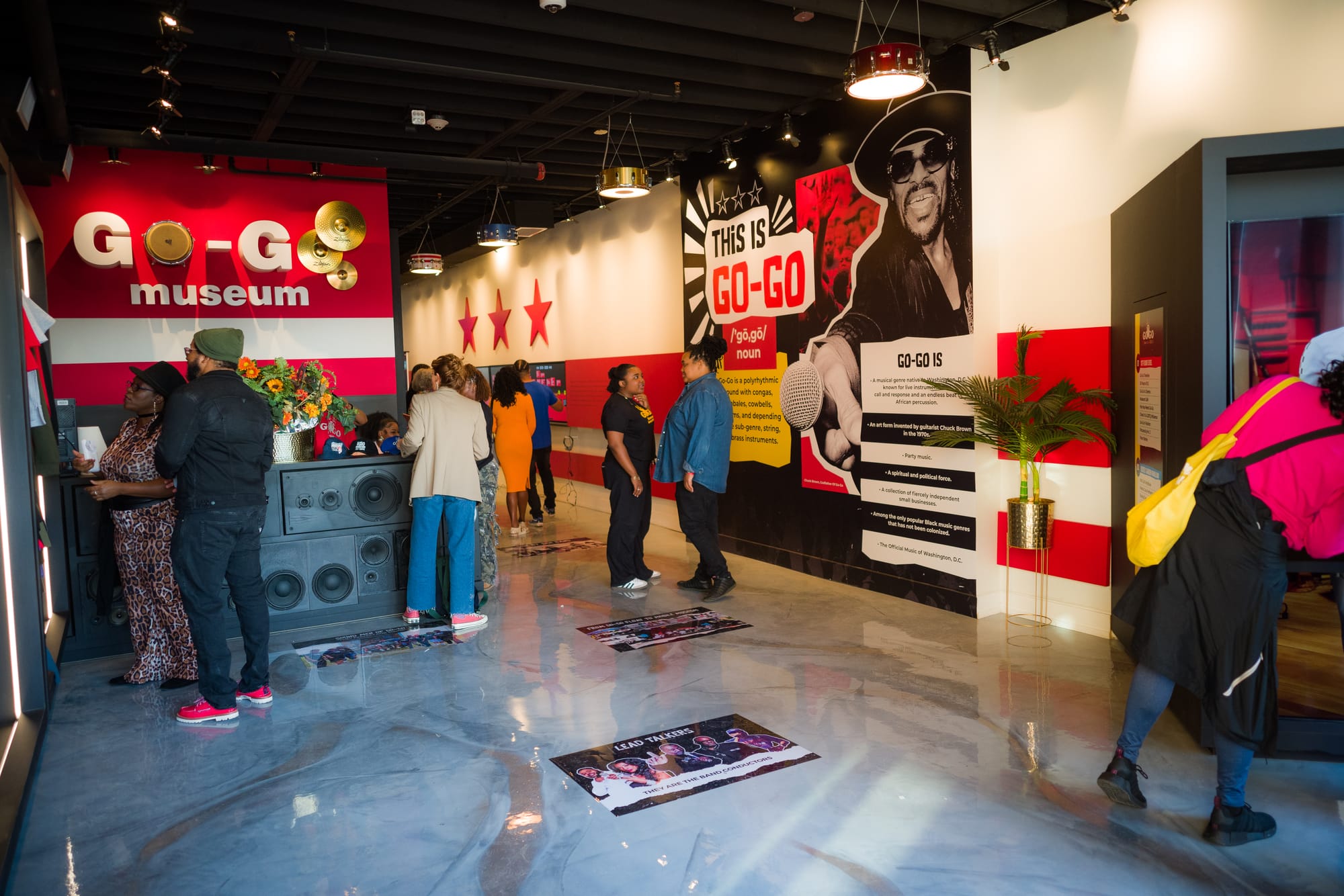 People stand around in the lobby of a large room with marble floors and red-and-white walls. 