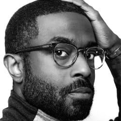 A black and white portrait of Shedrick looking directly at the camera with his hand on his forehead.