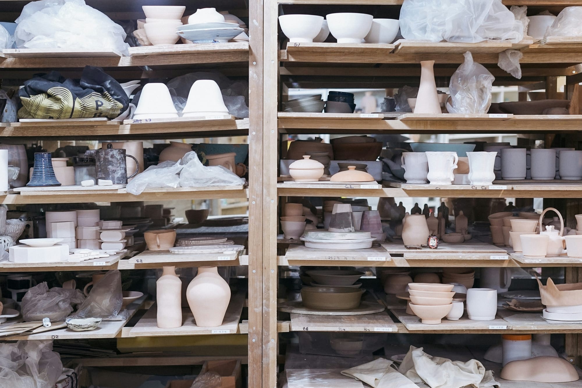 An image of drying ceramic cups, bowls, vases, and other pottery waiting to glaze on a shelf.