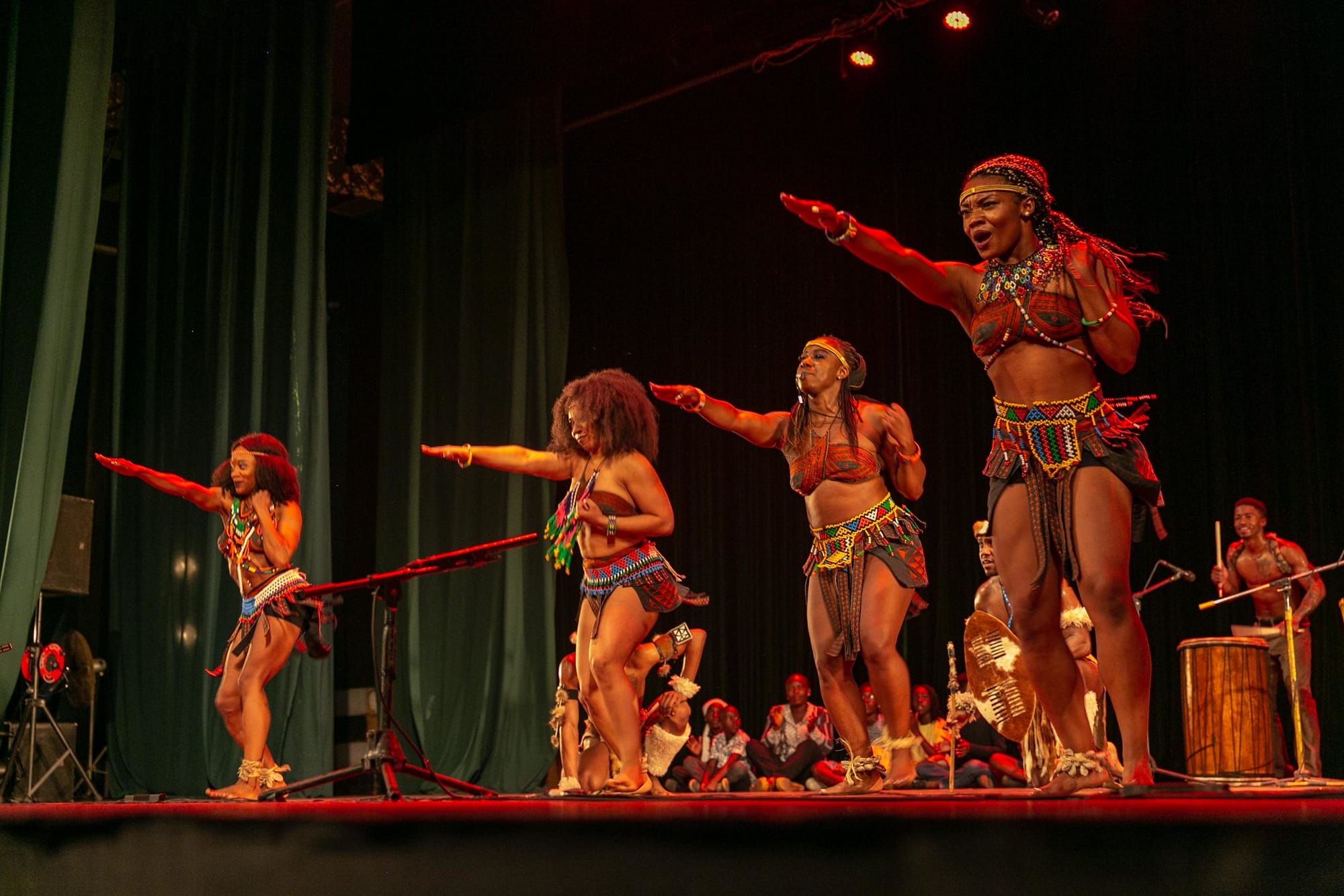 Performers with Step Afrika! onstage. Dancers in front lift their right arms straight ahead and drummers are visible in the back.