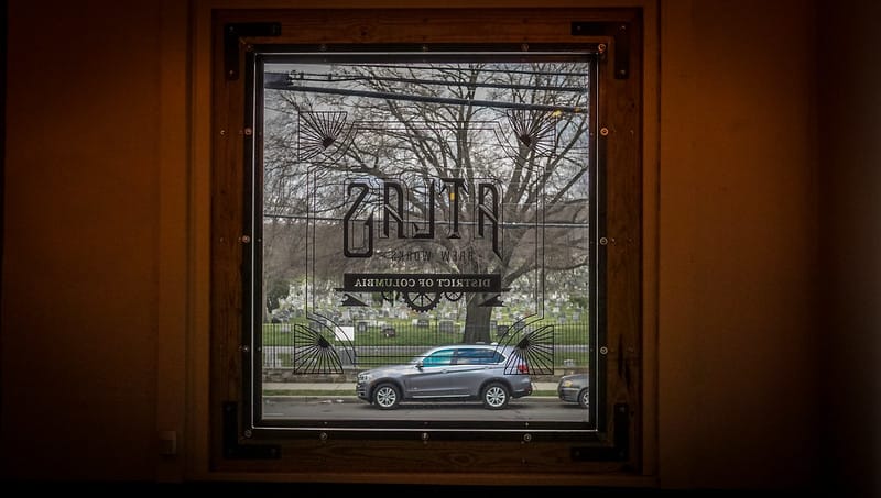 Image peering out of window on a dark brown door that reads Atlas District of Columbia.