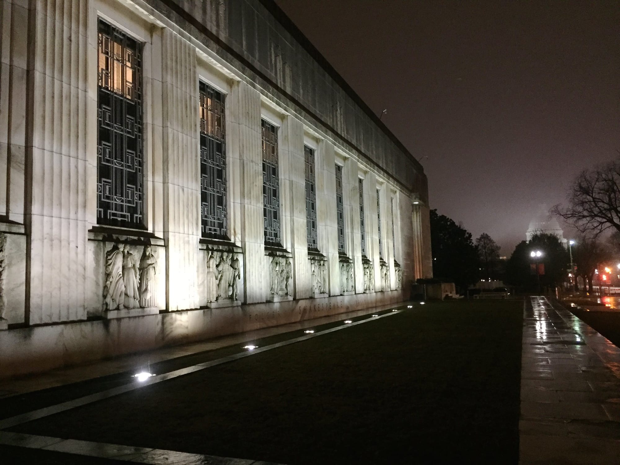 A view of the facade of Folger Theater at night. The Capitol building is also visible in the fog in the background.