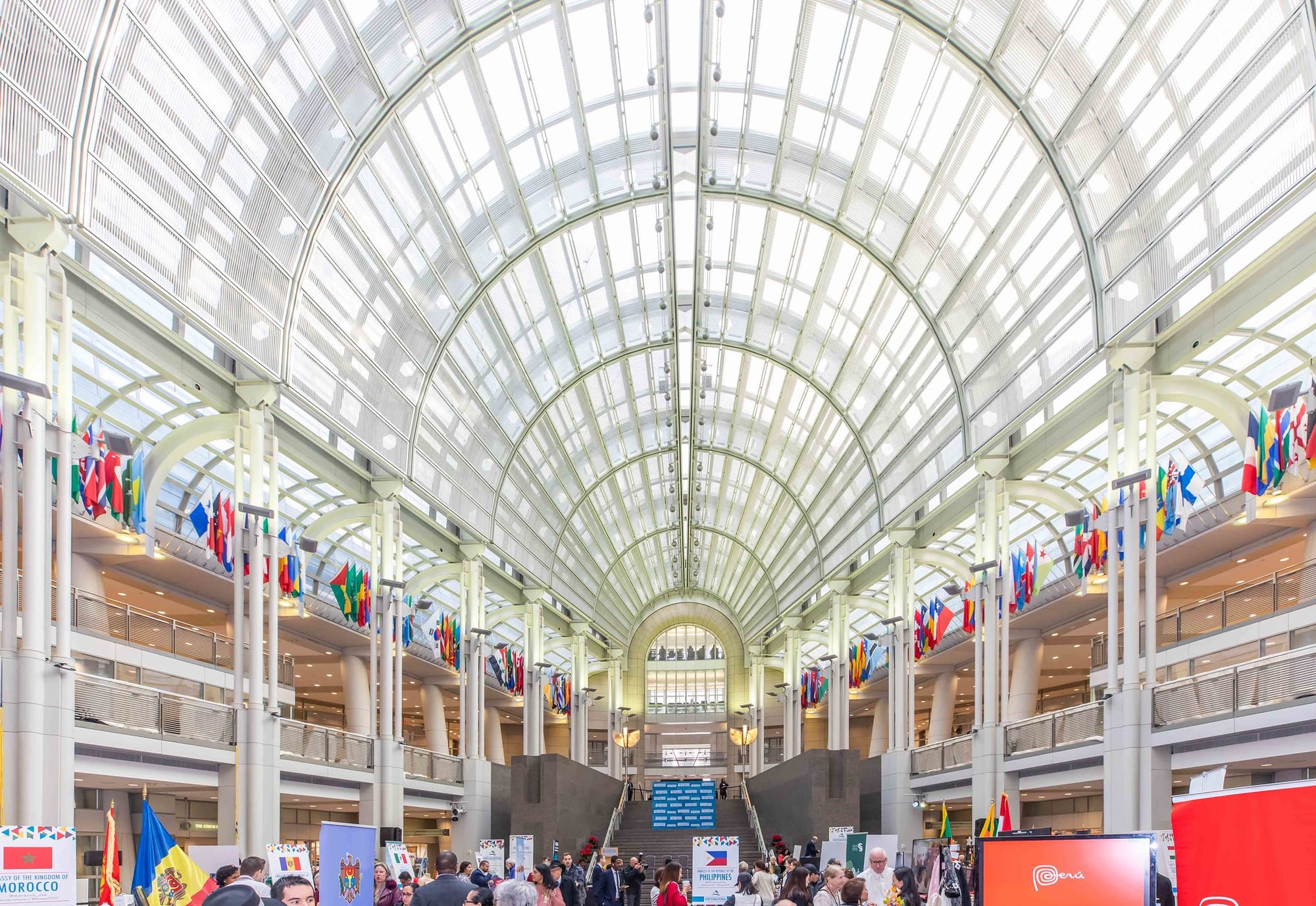 A large hall draped in flags, with people milling about a festival below. 