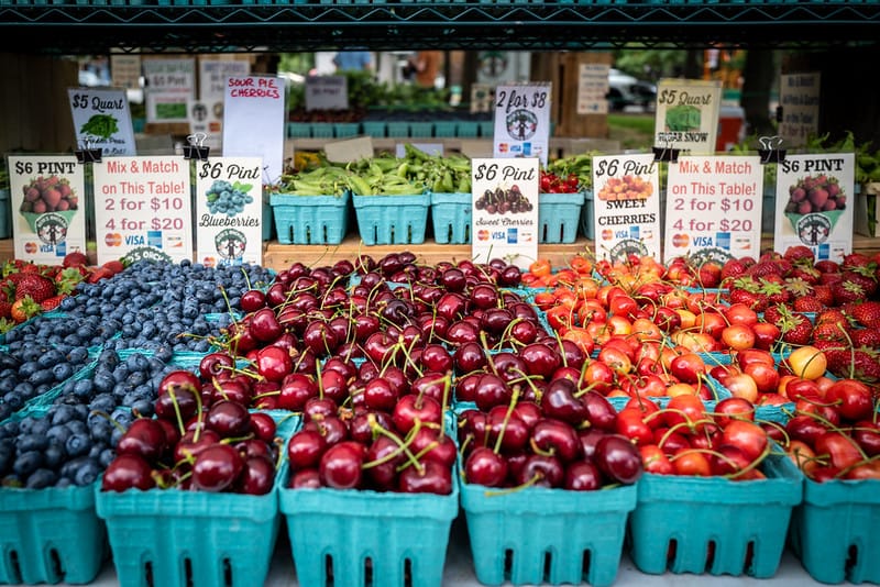 Blueberries, cherries, and vegetables at a farmers market stand.