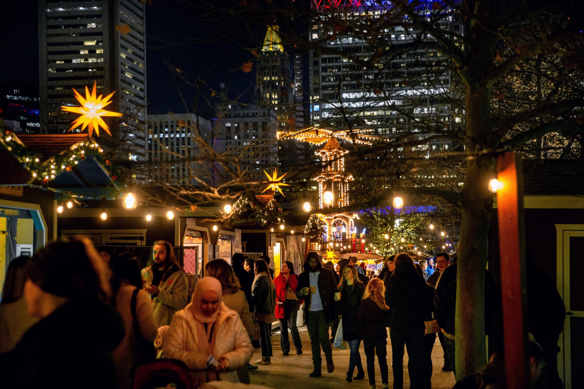 A crowd stands under twinkly lights at the Christmas Village in Baltimore.