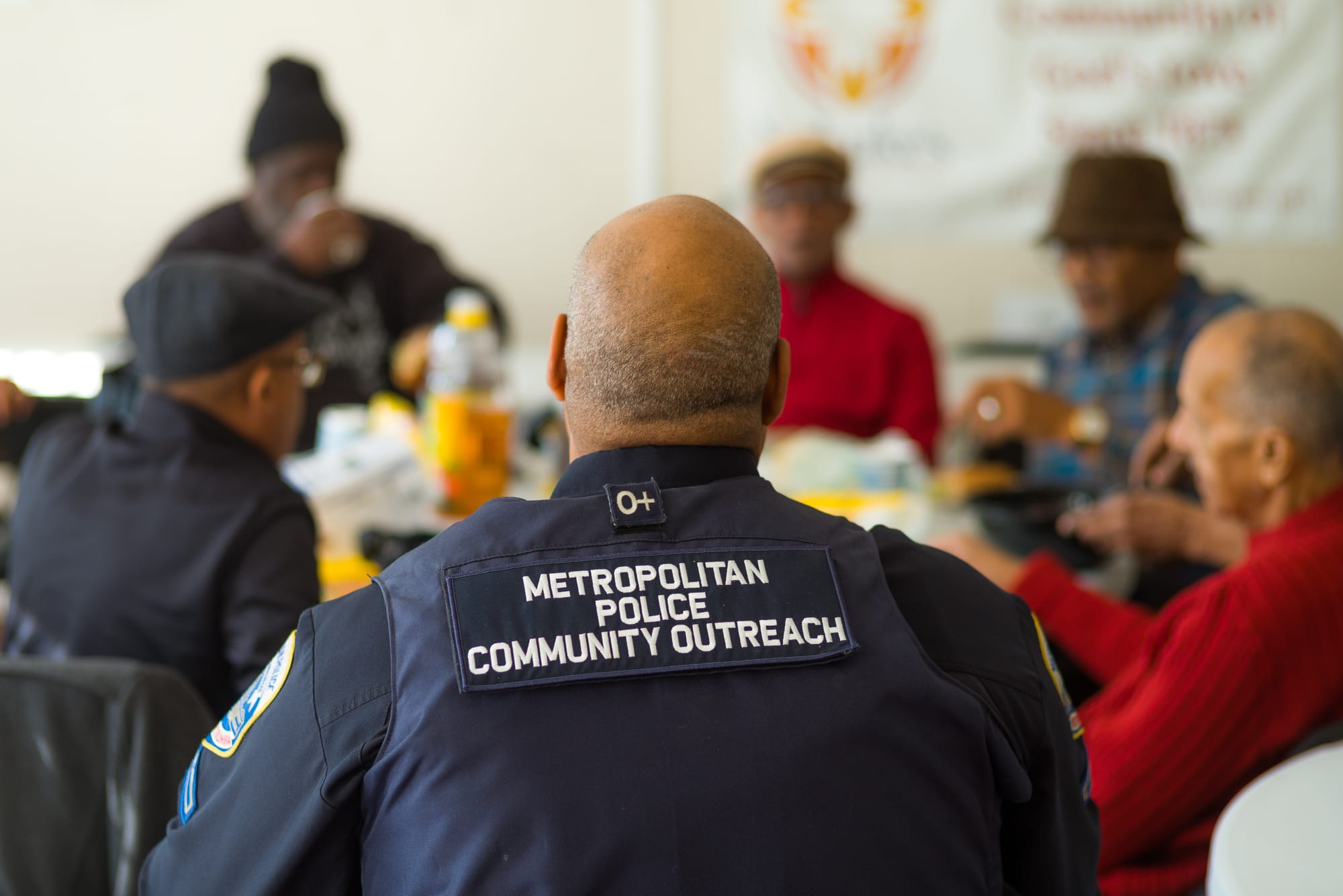 The back of a police officer with five men around a table in the background.