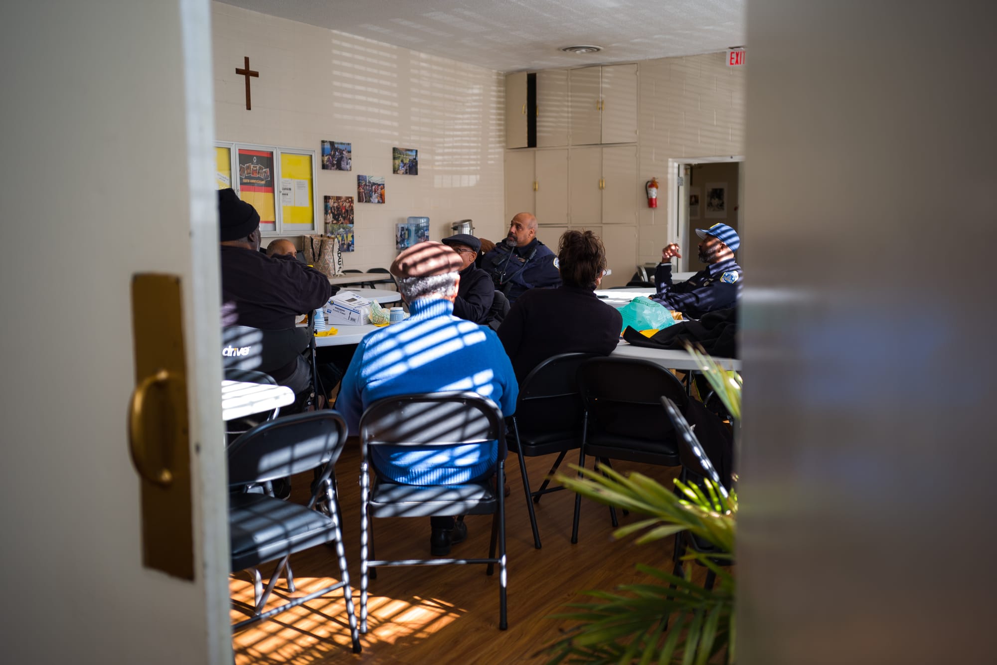 A group of men, mostly facing away from the camera, sit around tables at a church.