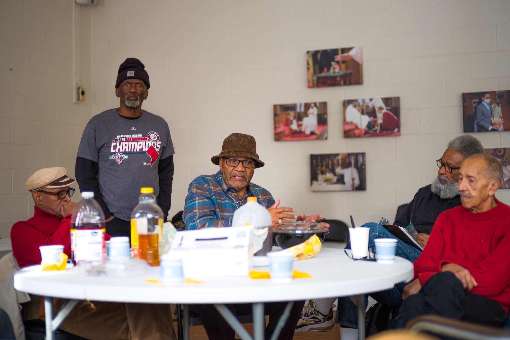 Five older Black men sit around a table having a discussion.