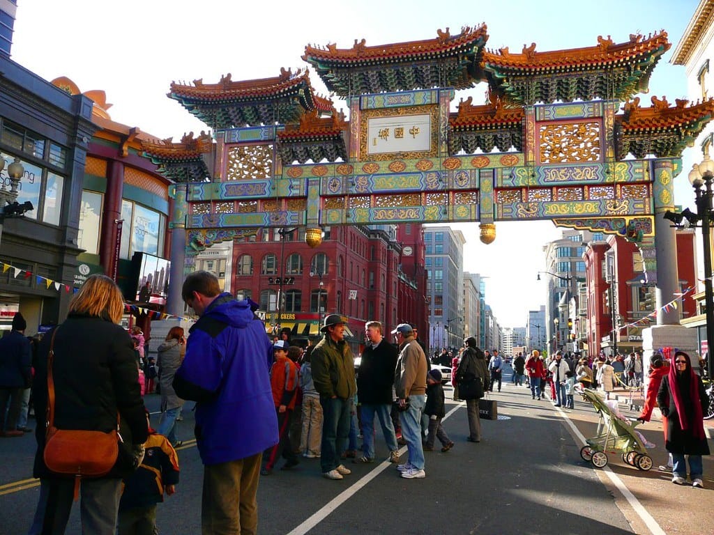 A crowd stands beneath the arches in Chinatown on a sunny day.