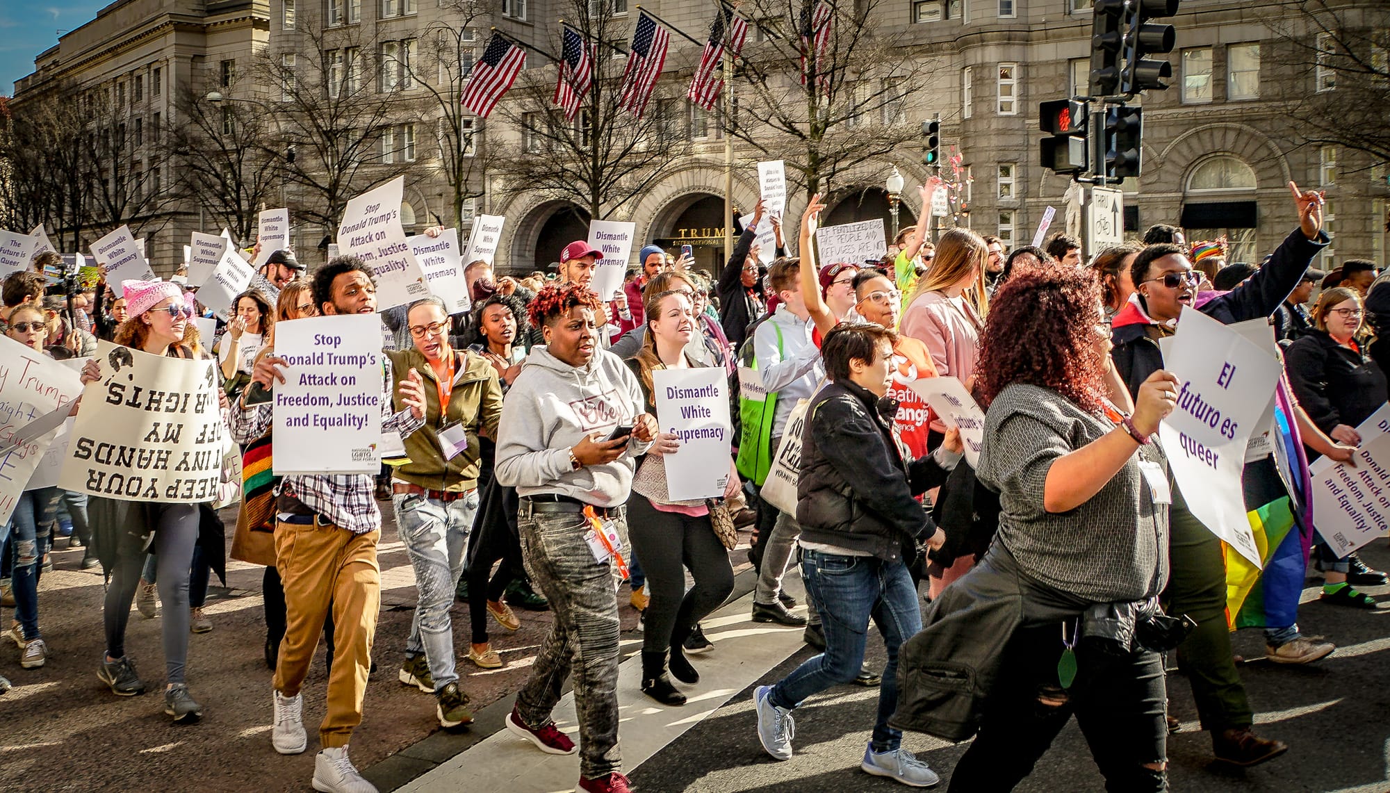 A queer dance protest marches down the streets of D.C. with dozens of people holding signs and raising their hands.