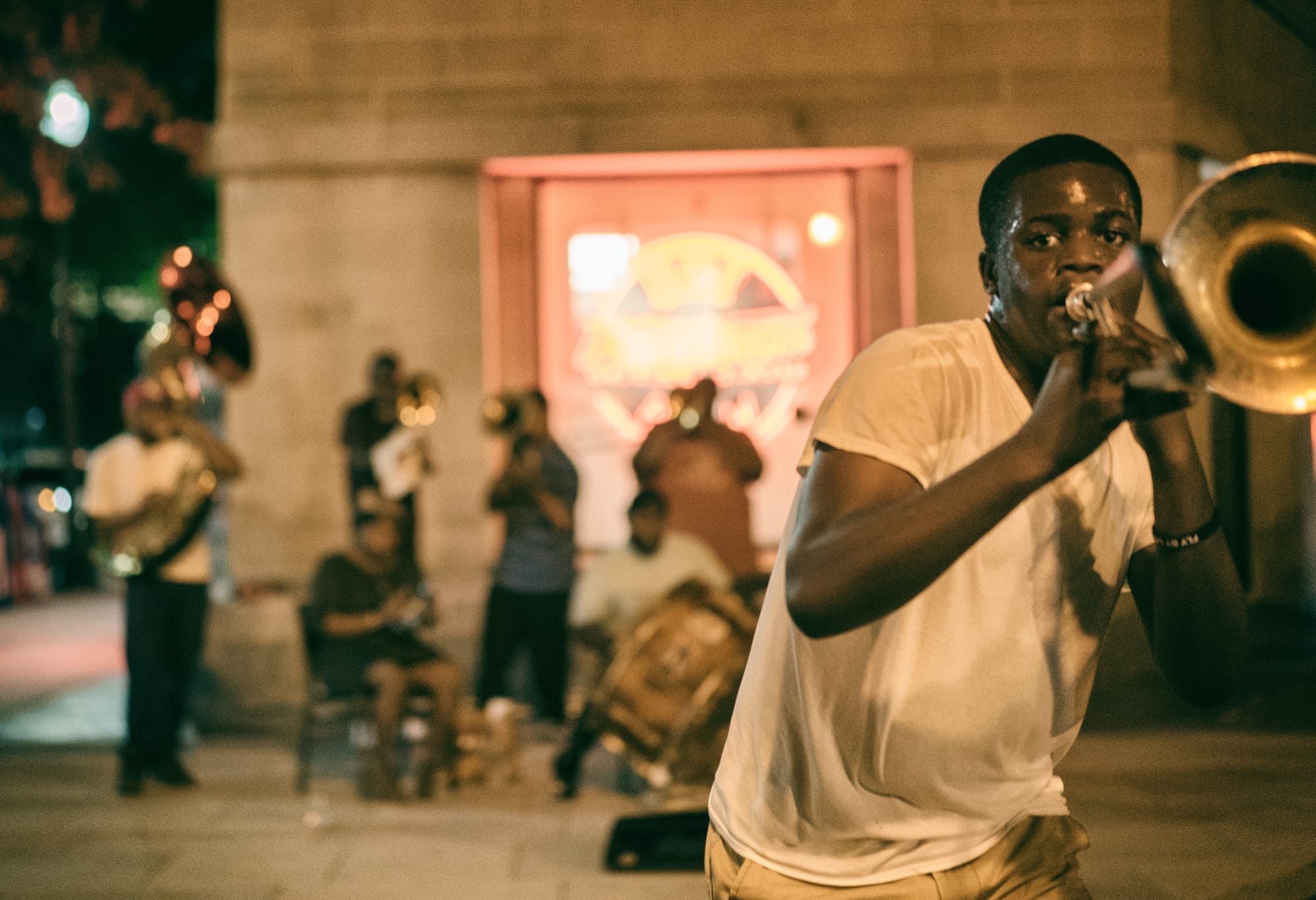 A person in the foreground plays the trombone while a large band playing various instruments plays in the background.