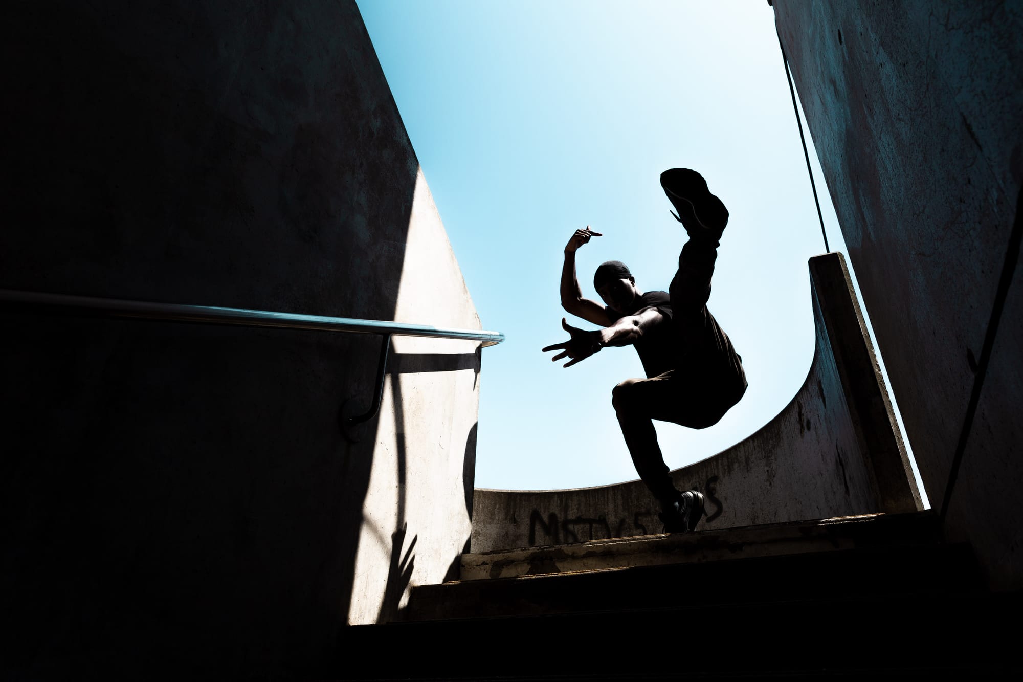 A Krump dancer strikes a post at the top of a shadowy staircase.