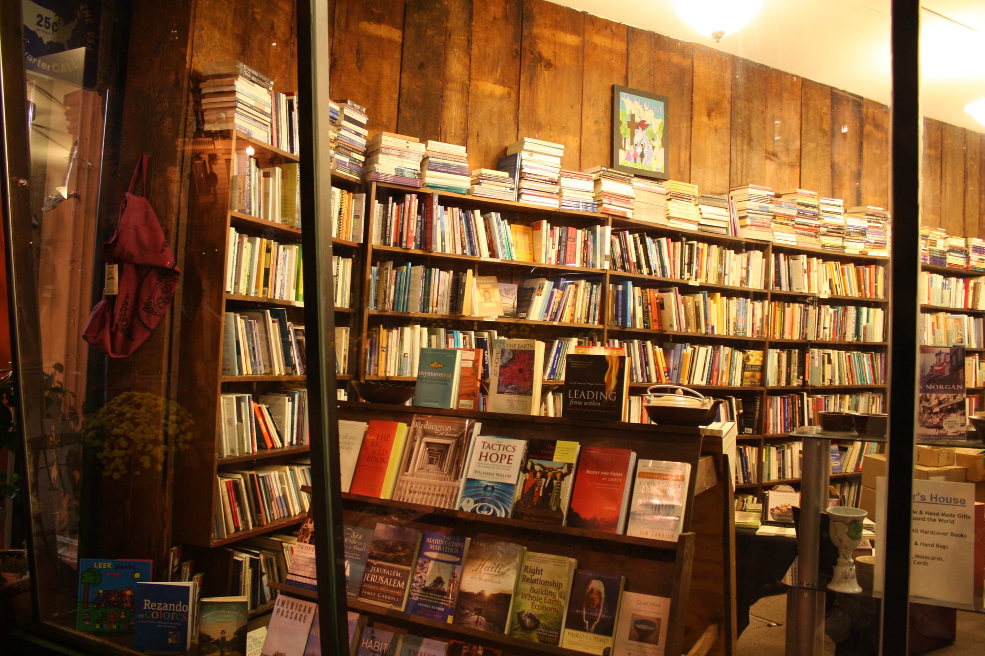 A photograph of a bookstore taken from outside the window with rows and rows of bookshelves in warm lighting.