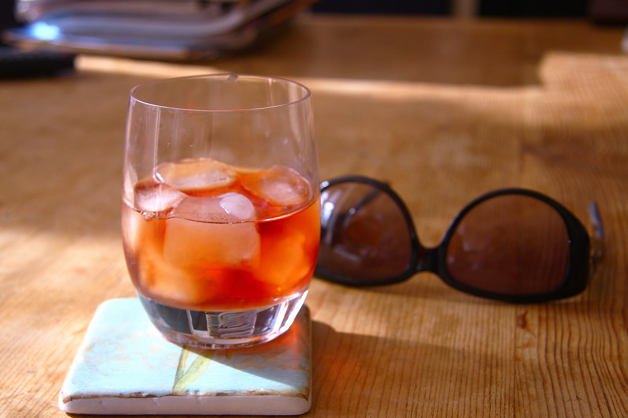 A half full cocktail on a coaster and sunglasses on a table.