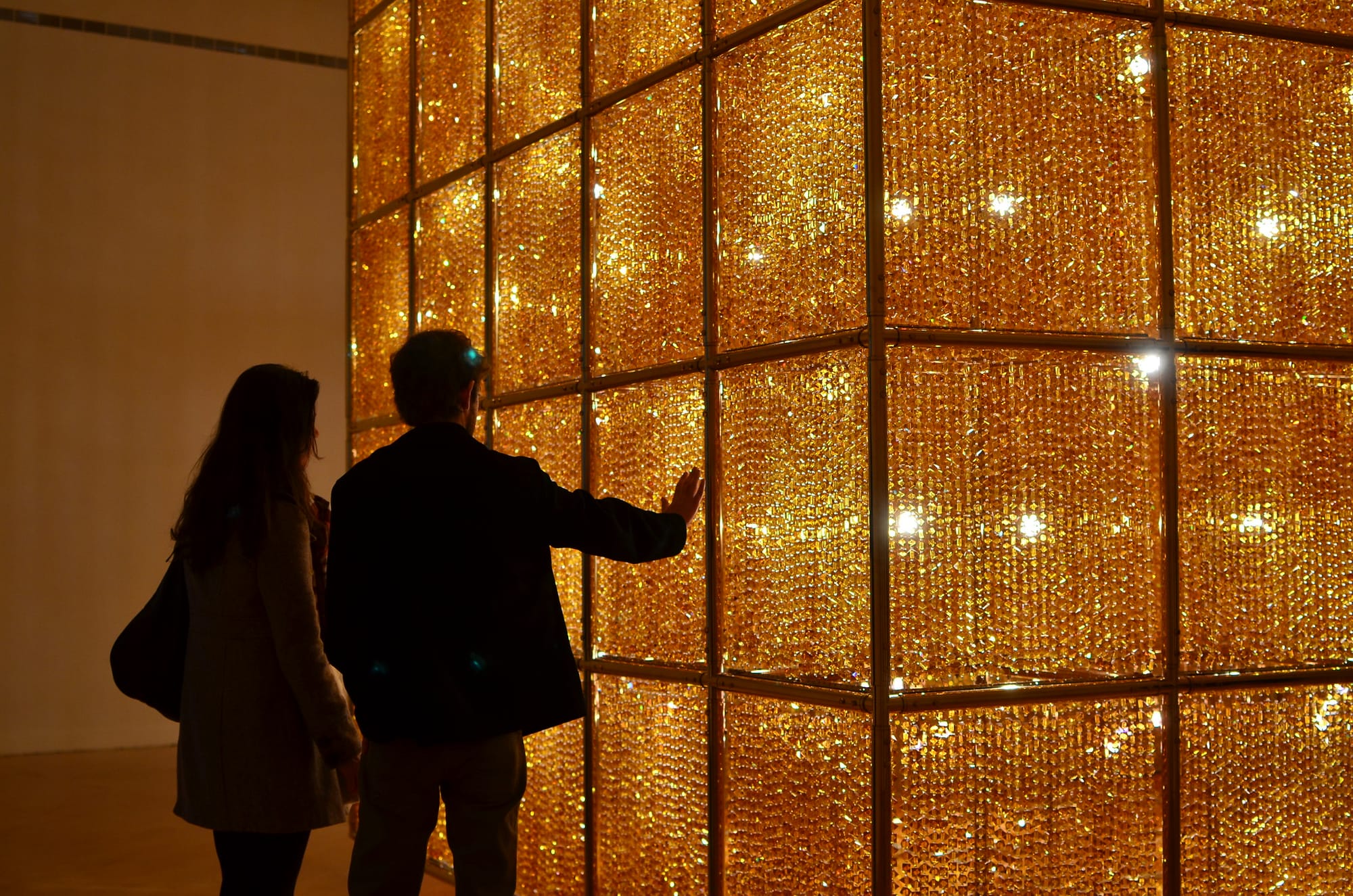 Two people stand with a hand pressed against a glowing exhibit in a golden room. 