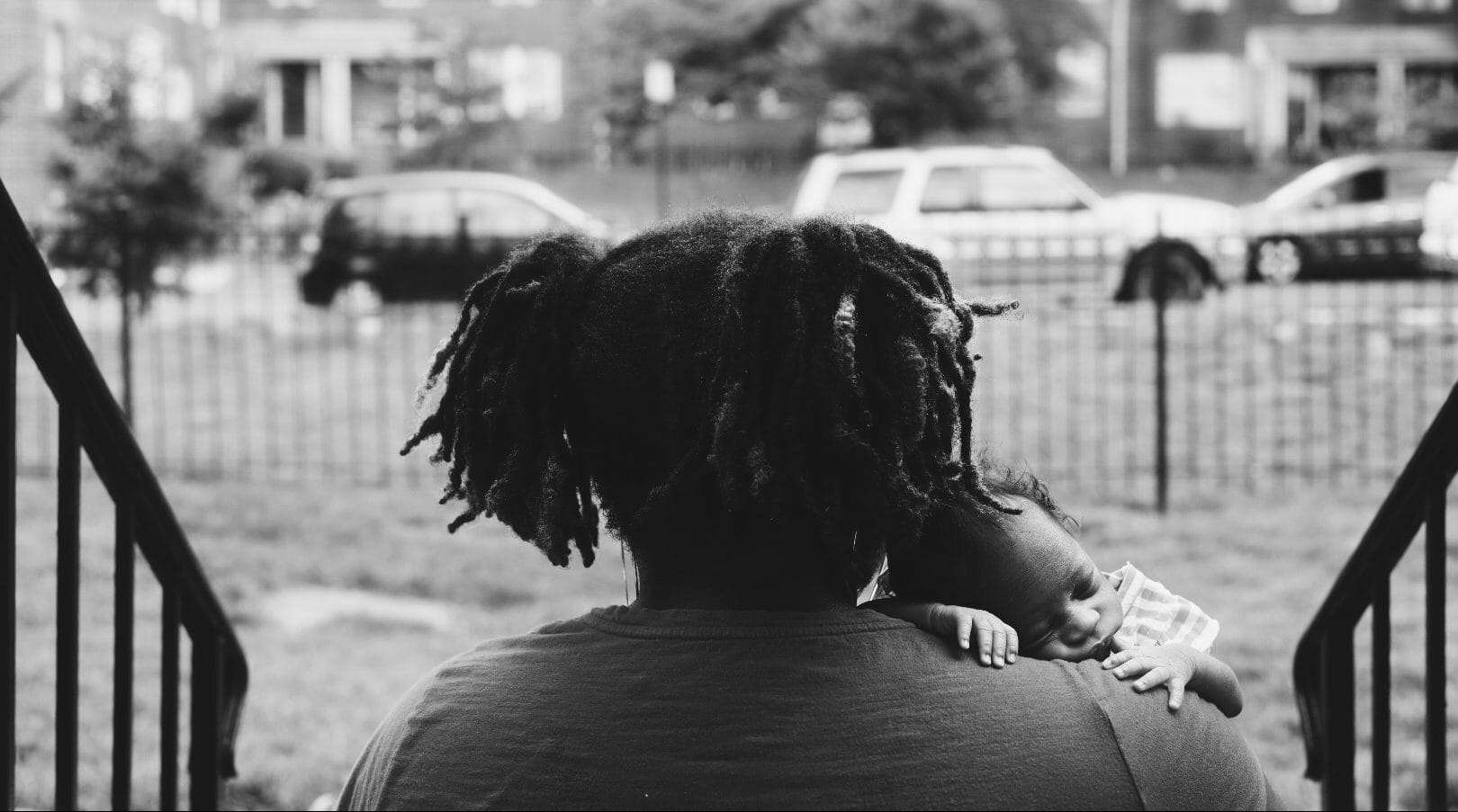 Black and white photo of a mother, with her back turned, holding a baby. 