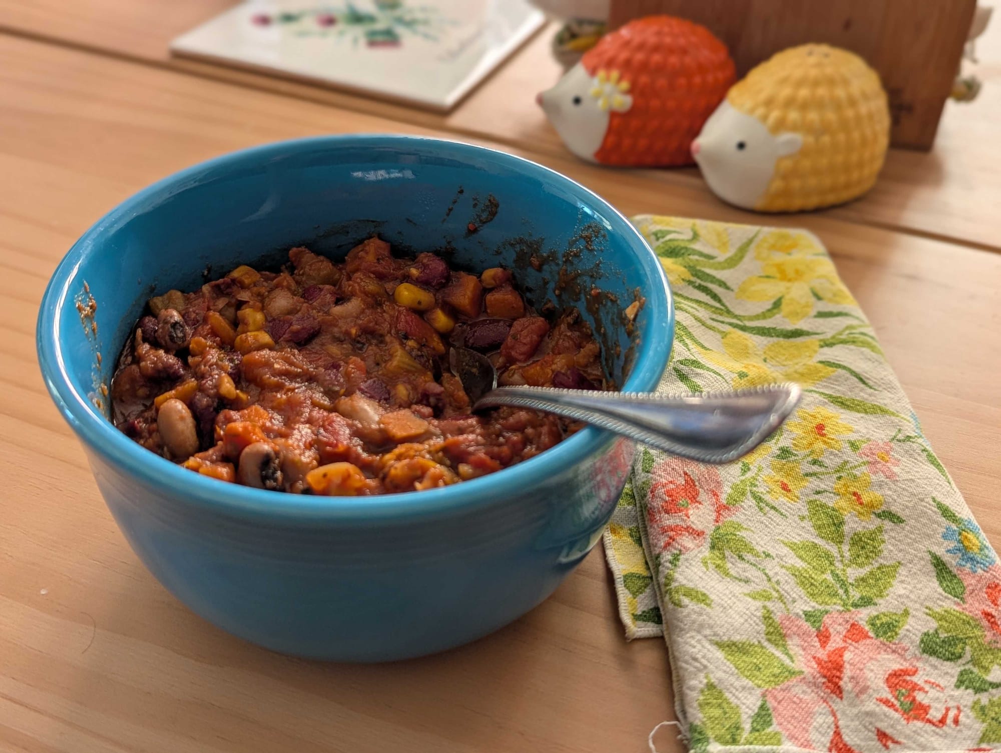 A blue bowl of chili with a floral napkin. 