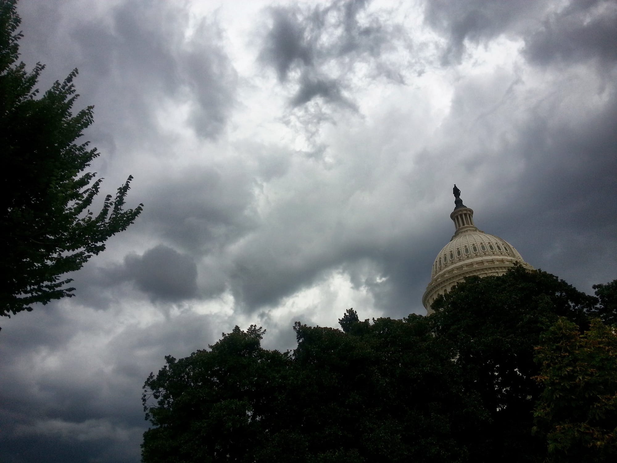 The Capitol building in Washington D.C. behind dark trees and clouds.