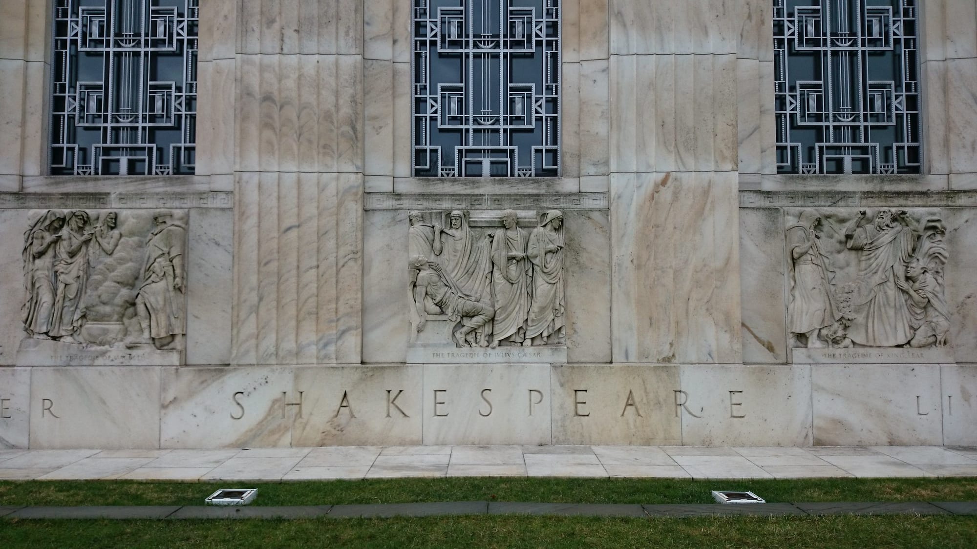 An outside of a marble building with Shakespeare carved in the side. 