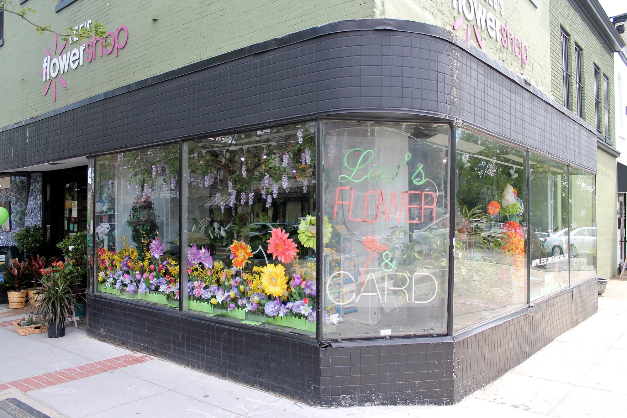 A photo of a green building on a corner, with lights in the window that read Lee's Flower & Card