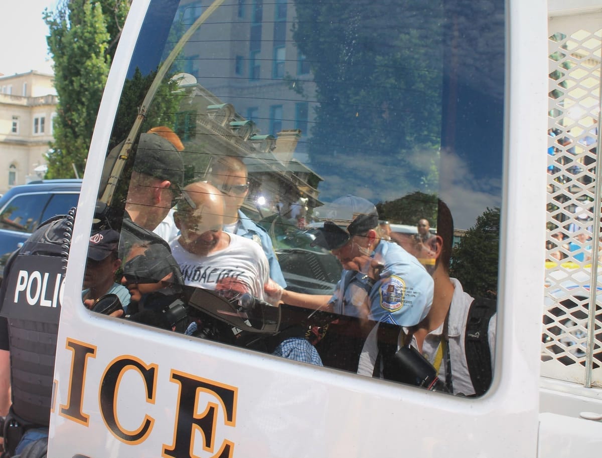  A photo of someone getting arrested, as seen through the rear window of a police vehicle.