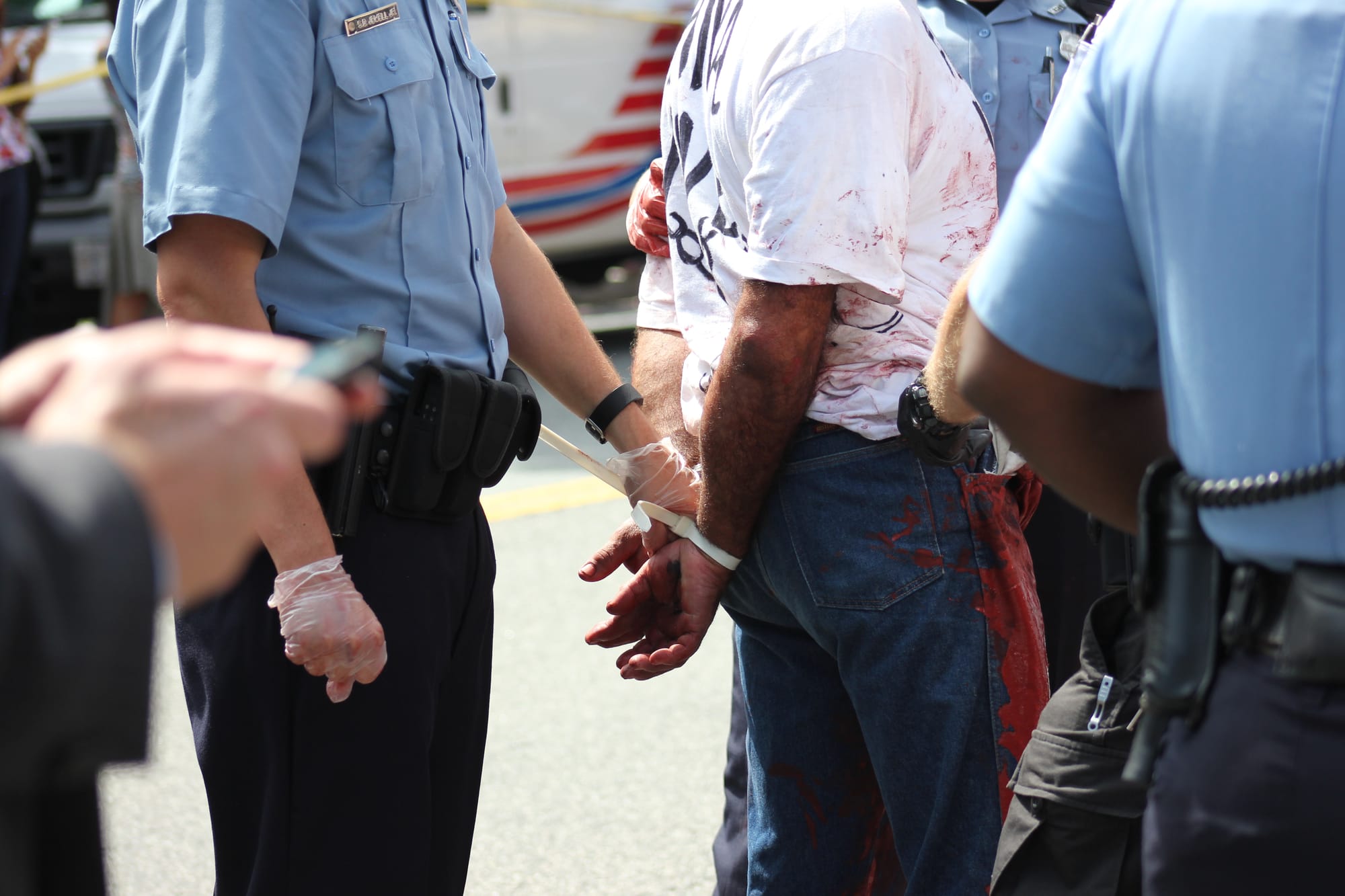 A photograph of police torsos and that of a person they're arresting, whose hands are zip tied behind their back.