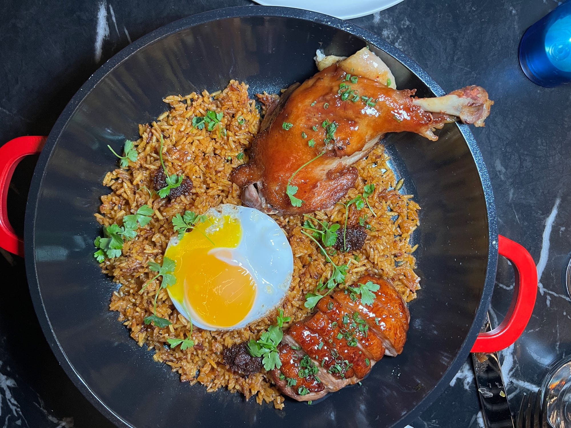 A picture of a pot of jollof rice with half an egg and a duck thigh.