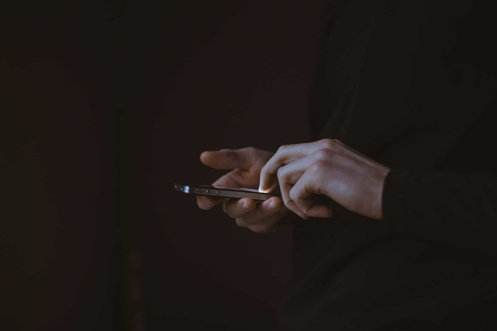 A photograph of hands holding an iPhone with a totally black background.