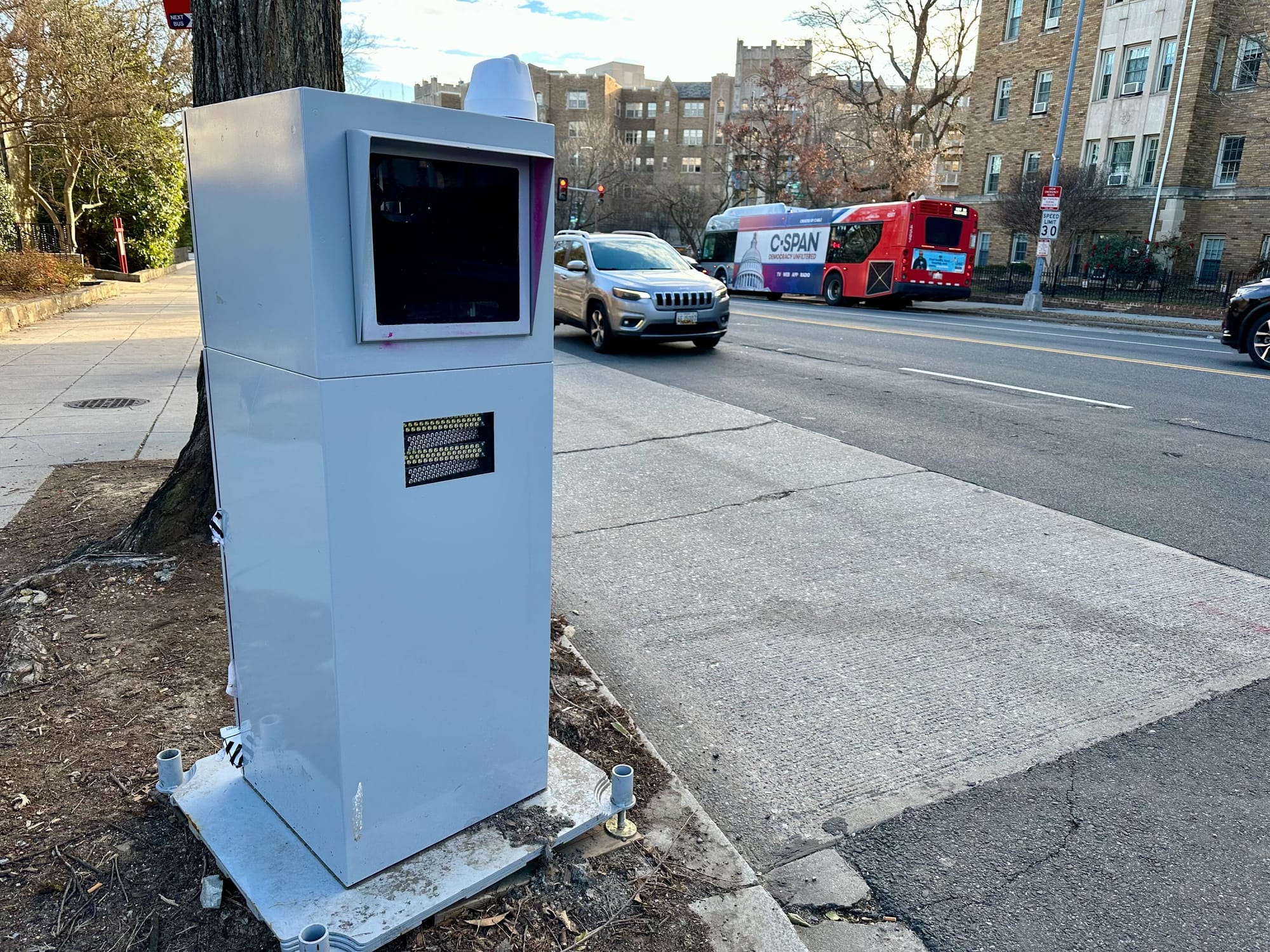 A picture of a traffic camera on the side of the road in D.C., with a car and a bus in the background.