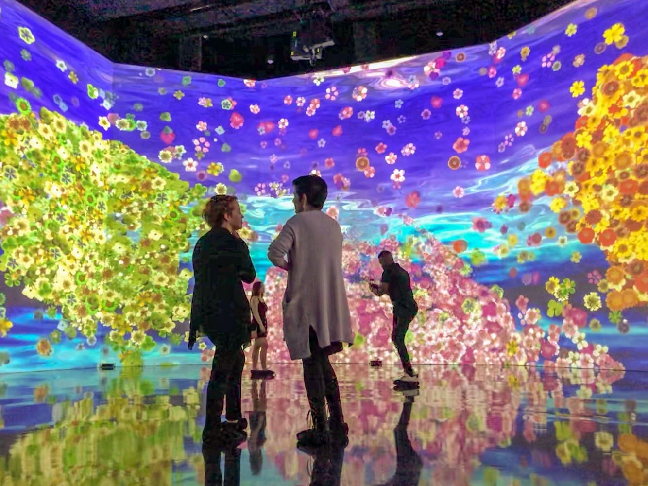 A couple stands on a large floor surrounded by a screen of vibrant floral colors. 