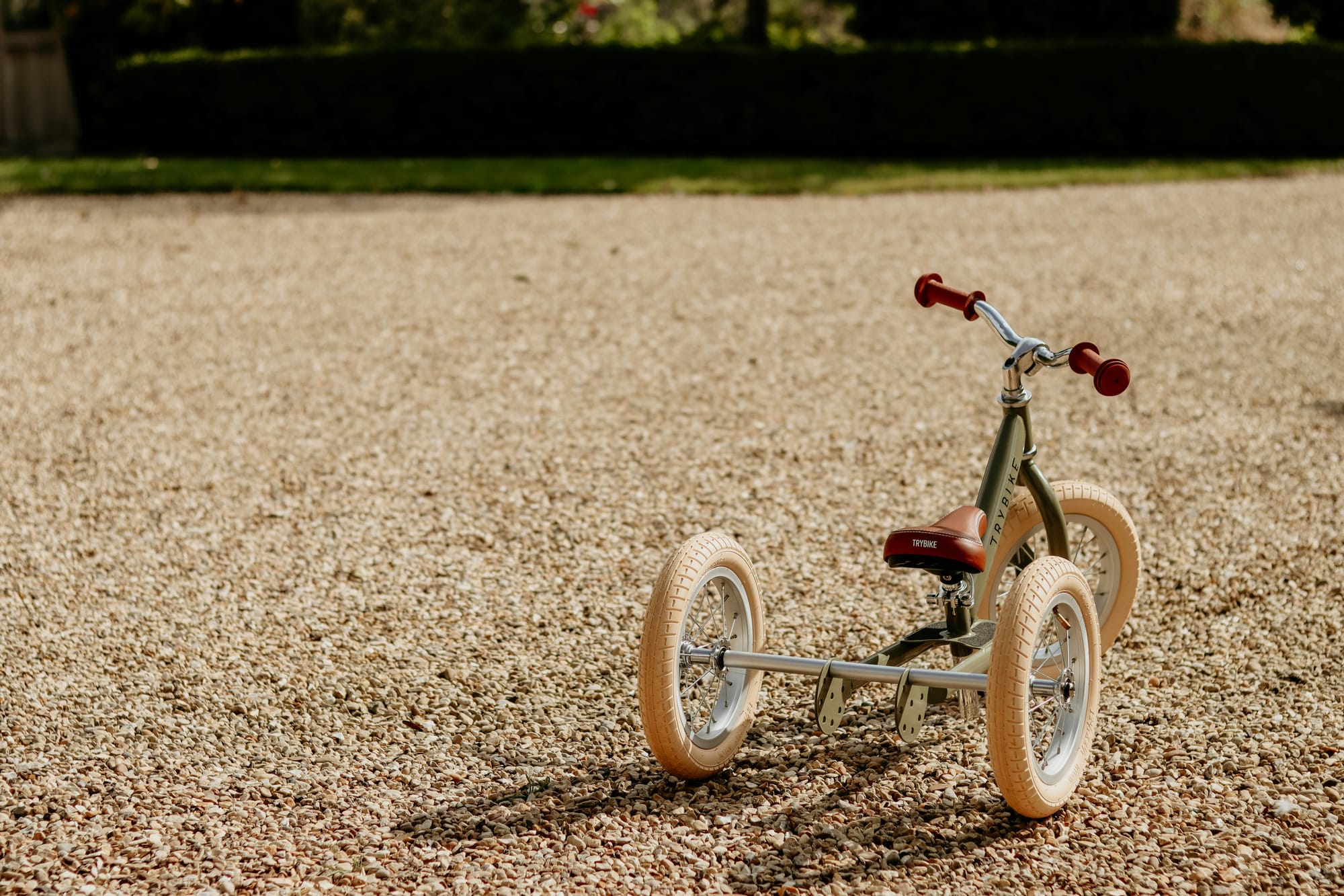 A red tricycle with white wheels sits in gravel.