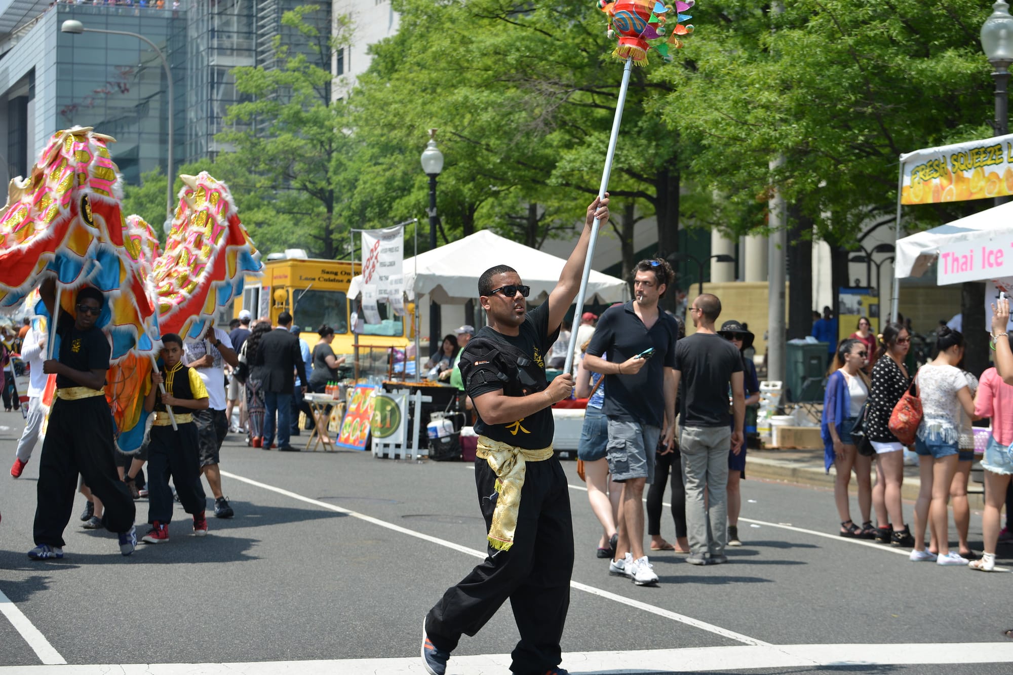 A man holds a pole in the air in the middle of a street fair.