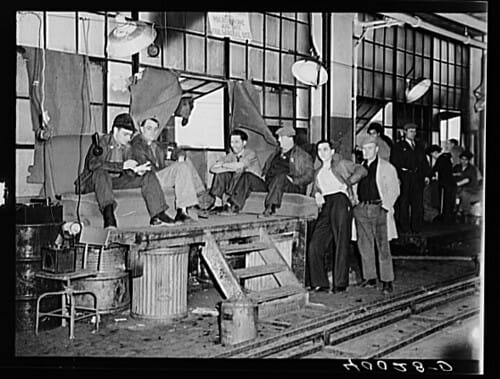 Old photograph of men sitting around a warehouse.