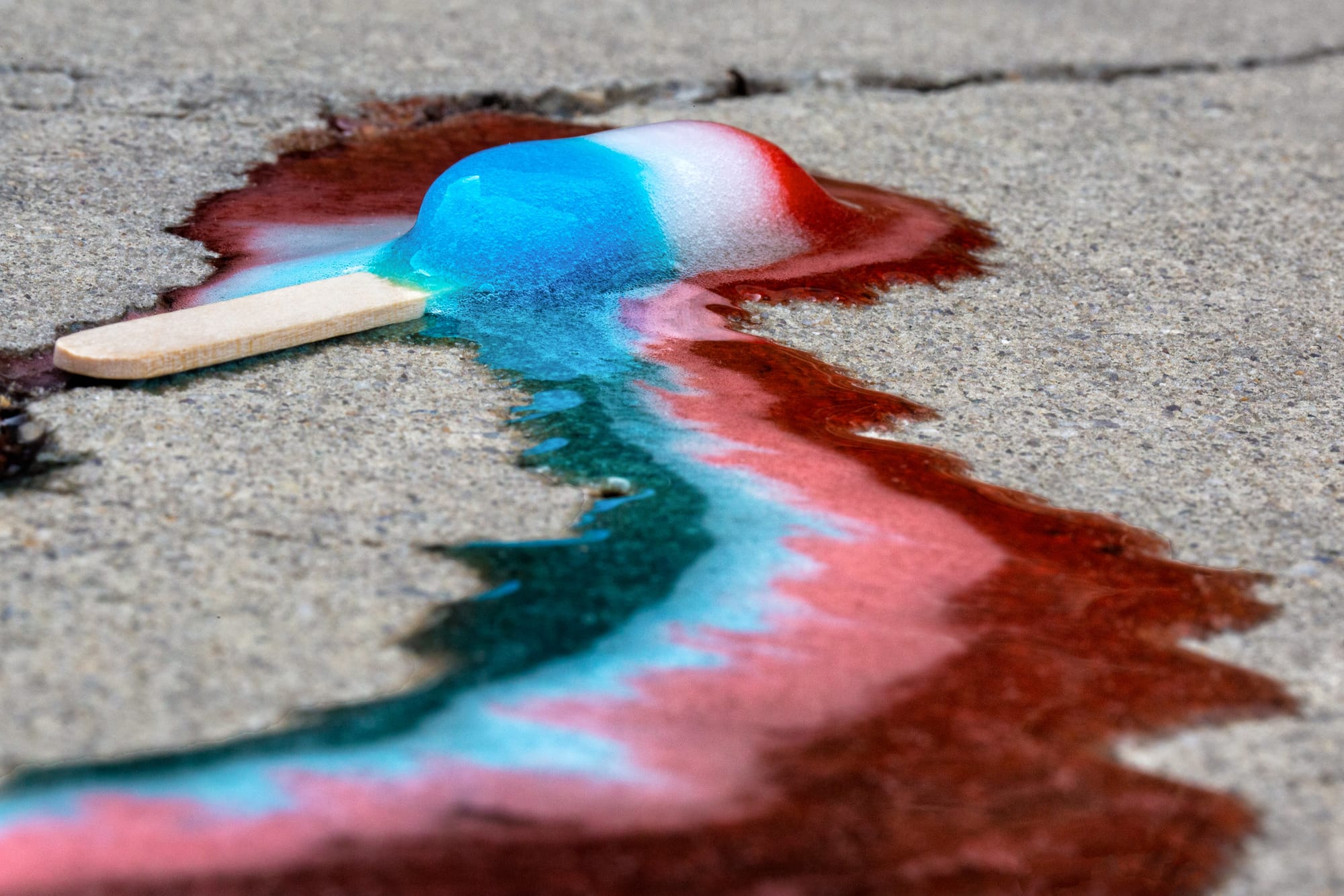 A red, white, and blue popsicle melting on a sidewalk. 