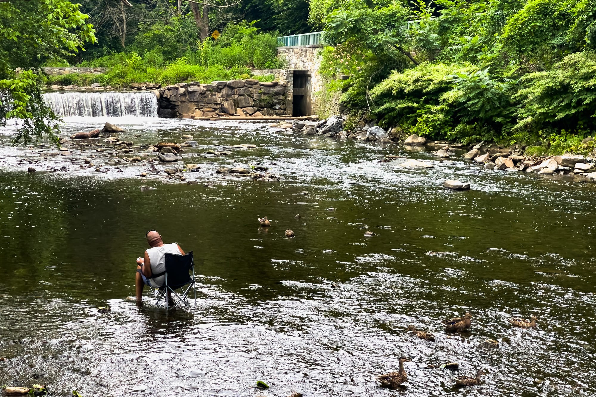 A man sitting in a folding chair in a creek with his feet in the water. 