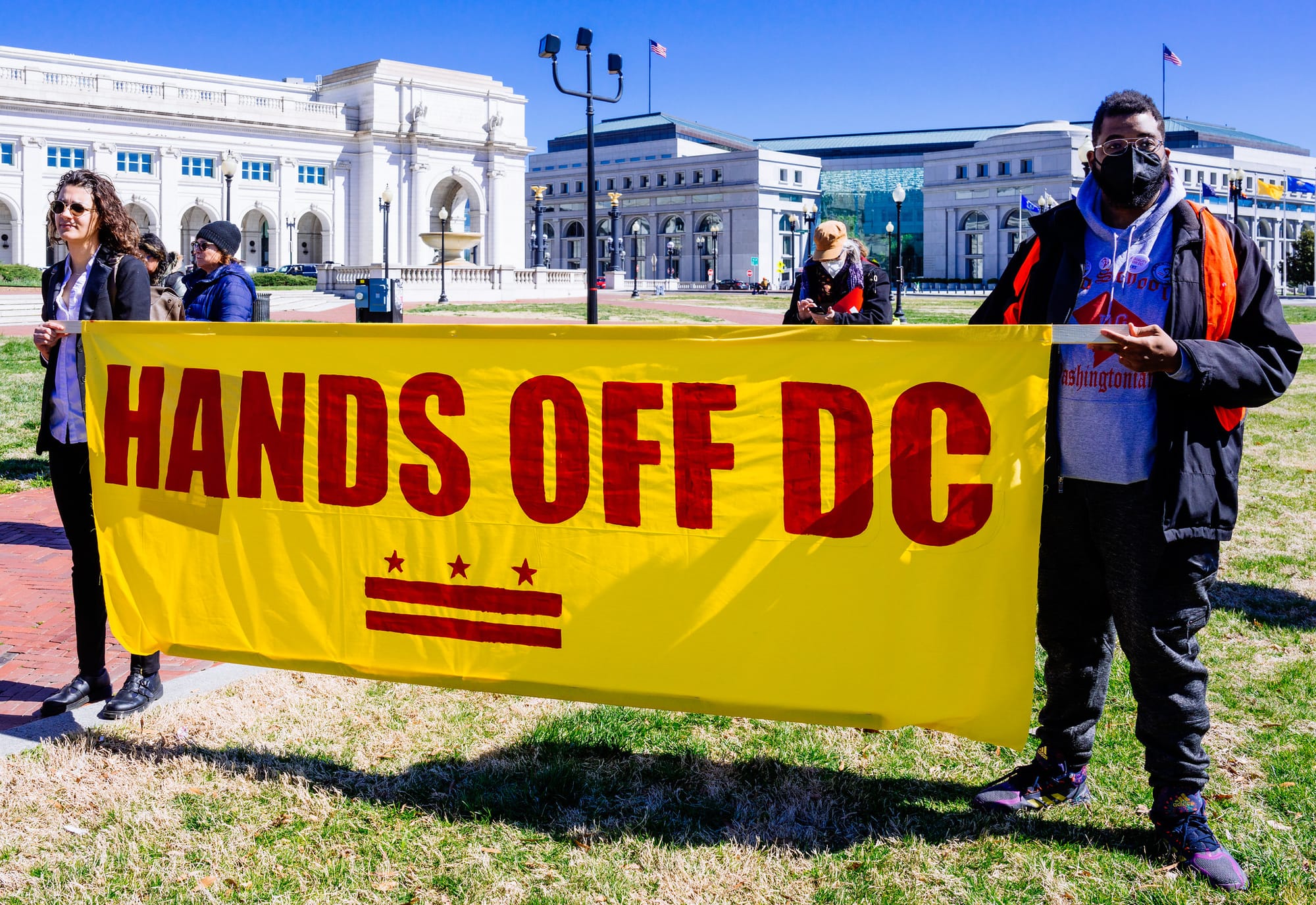 Two people holding a banner that reads Hands Off D.C. 