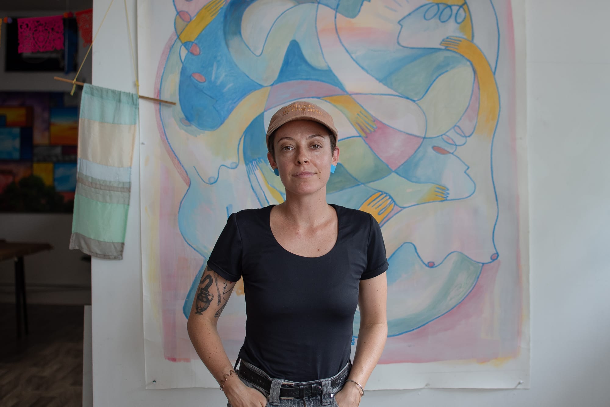 Photo of woman in a black t-shirt and brown hat standing in front of a painting.