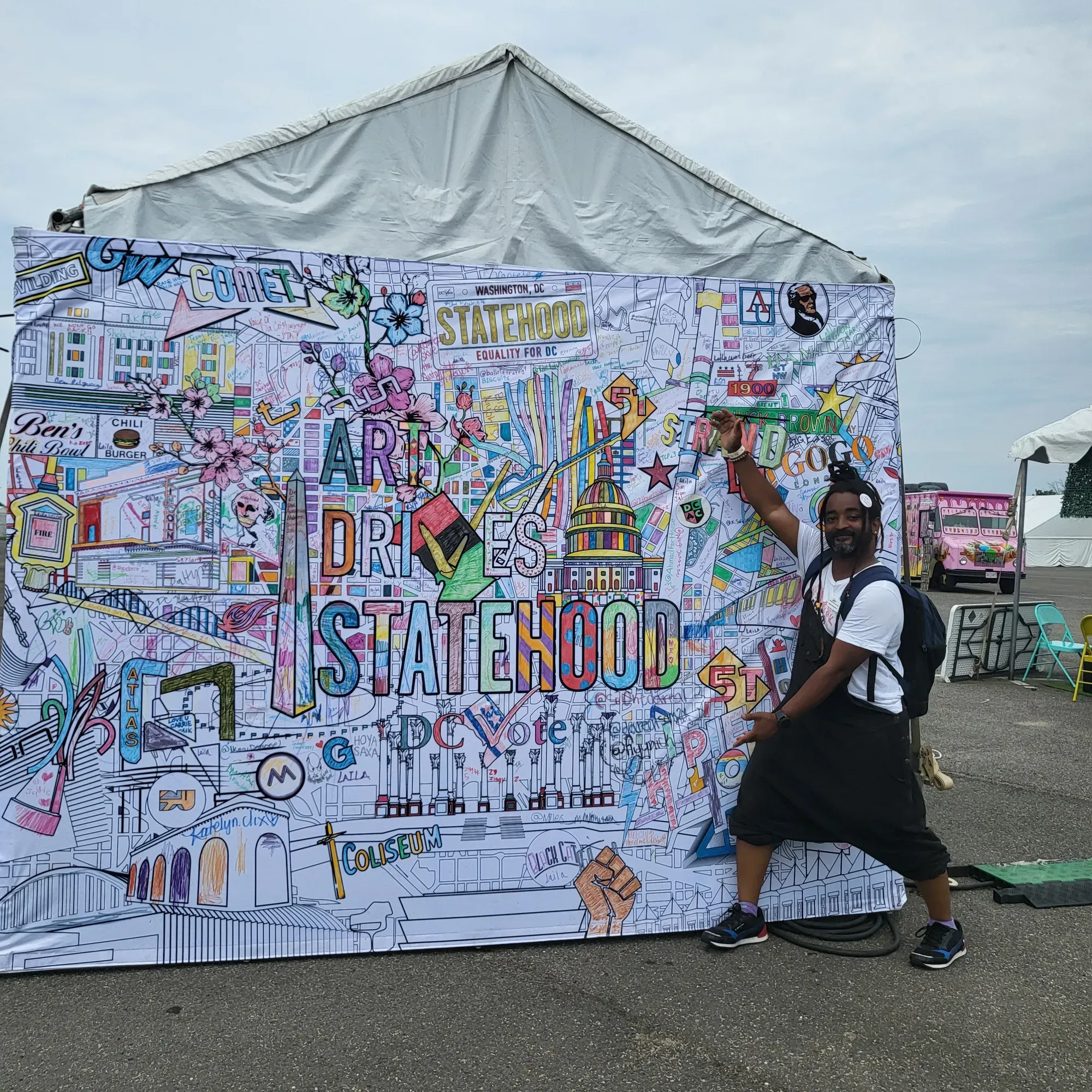 A person stands in front of a pop-up mural that reads "Art Drives Statehood" featuring D.C. iconography.